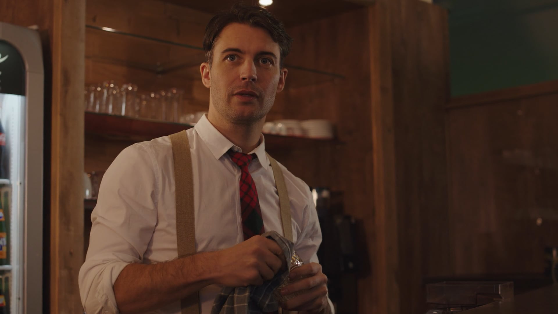 Barkeeper mit weißem Hemd, Hosenträgern und roter Krawatte hinter einer Bar