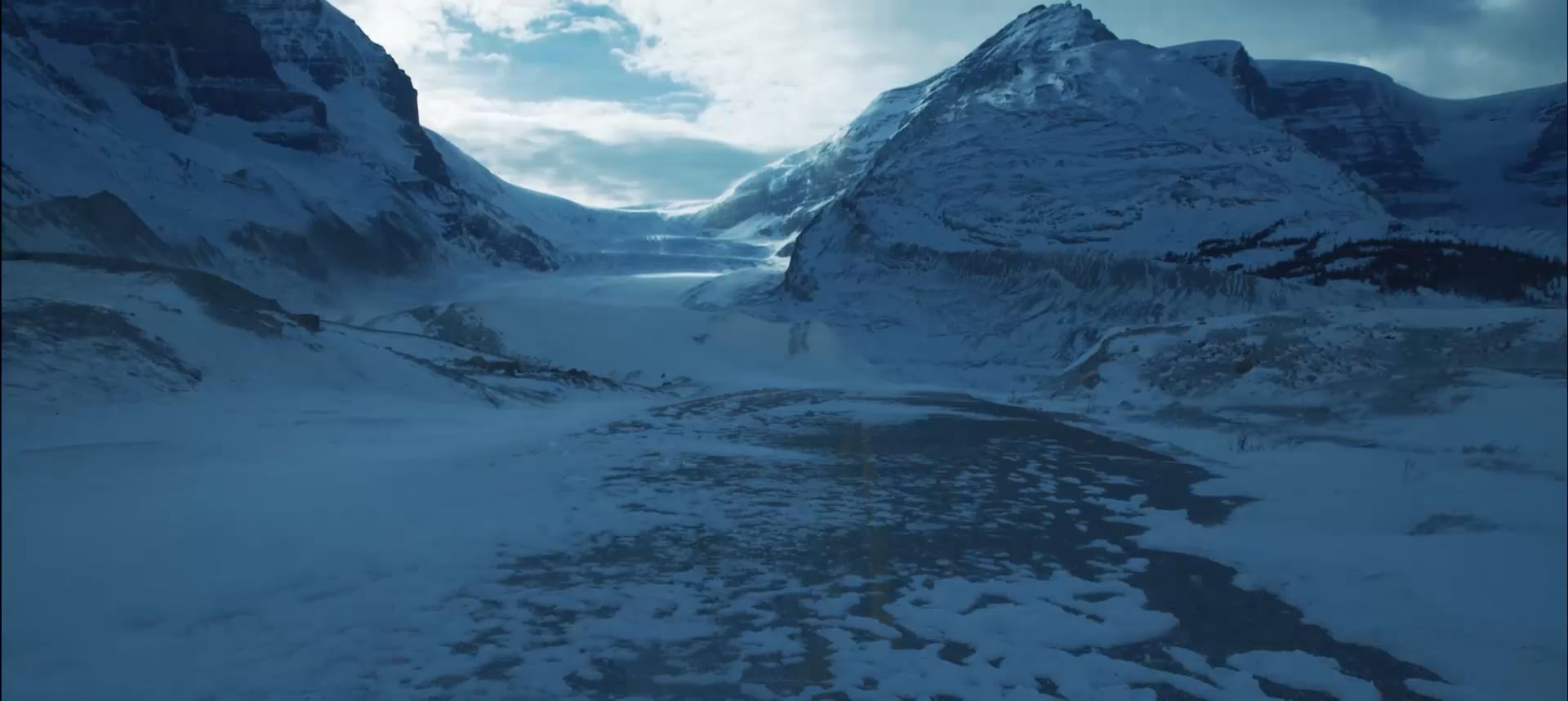 Weite verschneite Berglandschaft mit Gletscher, vereistem Flusstal und schneebedeckten Gipfeln