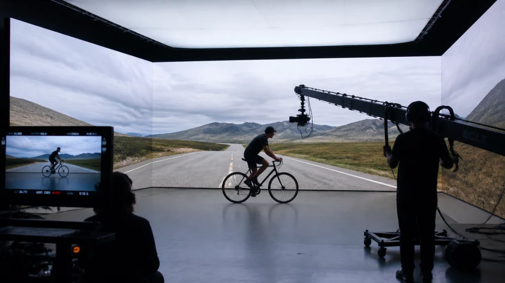 Filmcrew dreht einen Radfahrer vor einer großflächigen LED-Wand mit virtueller Straßen- und Berglandschaft